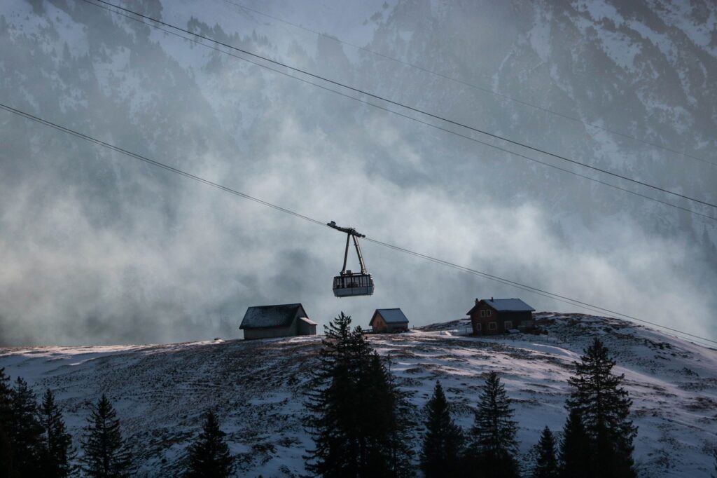 Gondelbahn inmitten einer nebeligen Berglandschaft fährt über eine kleine Siedelung auf dem Berg